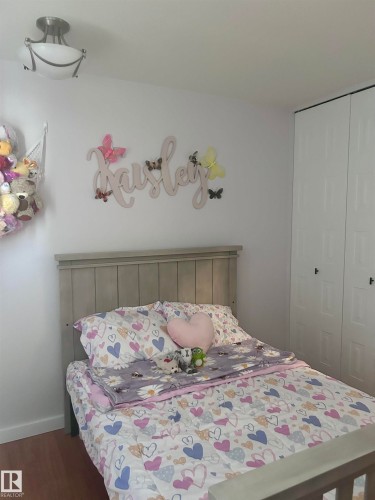 The room features a light-colored wooden bed frame, white walls, a flush-mount ceiling light, and white closet doors with dark handles - 4515 54 Ave, Tofield, AB - Indoor Photo Showing Bedroom