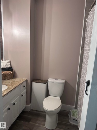 Bathroom featuring a vanity with a granite countertop and white cabinetry, a toilet, and wood-look flooring - 4515 54 Ave, Tofield, AB - Indoor Photo Showing Bathroom