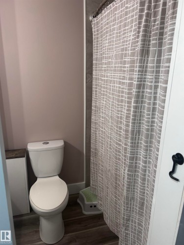 Bathroom featuring a white toilet, gray tiled shower surround, and wood-look flooring - 4515 54 Ave, Tofield, AB - Indoor Photo Showing Bathroom