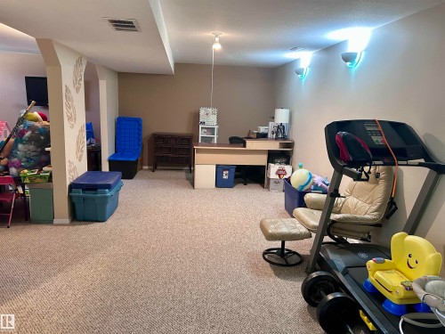 This expansive carpeted room features light-colored walls, recessed ceiling lighting, and decorative wall sconces providing ambient illumination - 4515 54 Ave, Tofield, AB - Indoor