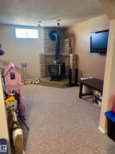 Spacious room featuring carpeting, a brick-surround wood-burning stove, and track lighting - 4515 54 Ave, Tofield, AB - Indoor With Fireplace