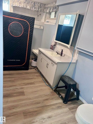 The bathroom features a vanity with a sink and storage, a wall-mounted medicine cabinet with a mirror, and light wood-style flooring - 4515 54 Ave, Tofield, AB - Indoor Photo Showing Bathroom