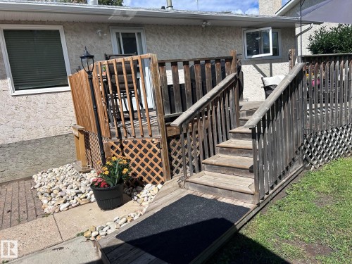 The property features an outdoor deck with wooden railing and steps, leading to a textured exterior wall - 4515 54 Ave, Tofield, AB - Outdoor With Deck Patio Veranda With Exterior