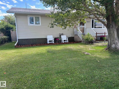 The property features a well-maintained lawn, mature trees, and a front entrance with white railings - 4515 54 Ave, Tofield, AB - Outdoor