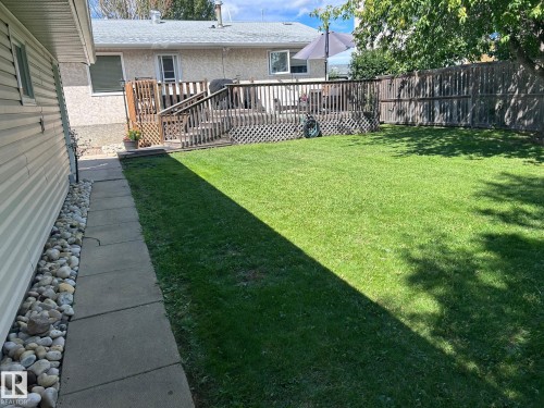 The property features an extensive lawn area, a wooden deck with railing, and a privacy fence - 4515 54 Ave, Tofield, AB - Outdoor