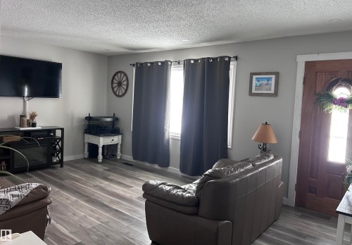 Inviting living area featuring wood-look flooring, light gray walls, and large windows with dark curtains - 4515 54 Ave, Tofield, AB - Indoor Photo Showing Living Room