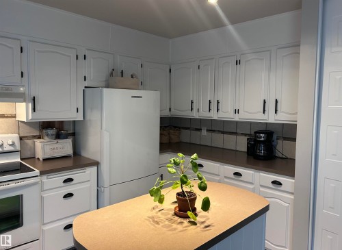 The kitchen features white cabinetry with black hardware, complementing the dark countertops and tiled backsplash - 4515 54 Ave, Tofield, AB - Indoor Photo Showing Kitchen