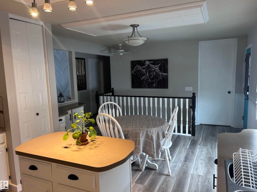 The kitchen area features grey plank flooring, a kitchen island with a light-colored countertop, and white cabinetry with dark hardware - 4515 54 Ave, Tofield, AB - Indoor Photo Showing Dining Room