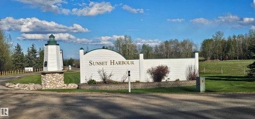 The property features an entrance with a white sign displaying "Sunset Harbour" and a lighthouse-style structure with a green roof, set against a backdrop of trees and a grassy area - #1 Sunset Harbour, Rural Wetaskiwin County, AB 