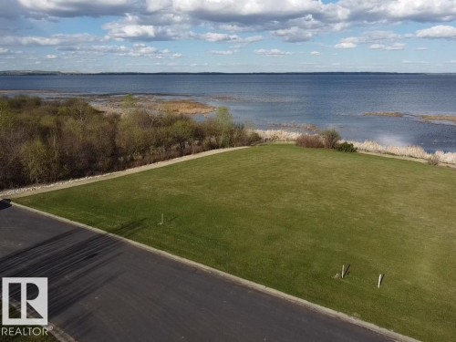 The property features a large grassy area with direct frontage to a body of water, offering expansive water views - #1 Sunset Harbour, Rural Wetaskiwin County, AB 