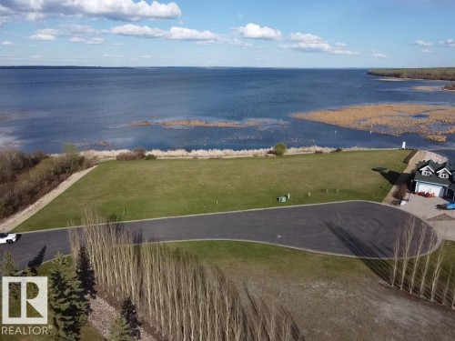 Expansive property featuring a large green lawn, a paved driveway, and established trees, all set against a scenic waterside backdrop - #1 Sunset Harbour, Rural Wetaskiwin County, AB 