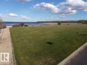 Expansive green lawn with a gravel pathway, offering views of the large body of water, partially lined with reeds and distant vegetation under a blue sky with clouds - #1 Sunset Harbour, Rural Wetaskiwin County, AB 