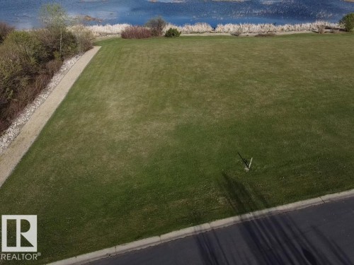 This property features a spacious grassy area bordered by a paved path and a roadway - #1 Sunset Harbour, Rural Wetaskiwin County, AB 