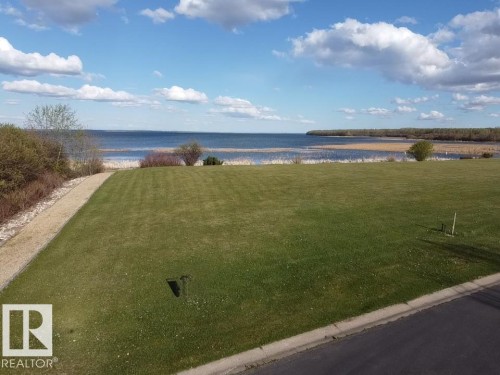 Expansive green lawn with a clear view of the water and distant treeline, offering a serene outdoor setting - #1 Sunset Harbour, Rural Wetaskiwin County, AB 