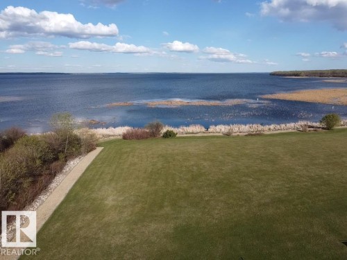 Expansive lawn area with a view of the lake, featuring a walking path and natural vegetation along the waterfront - #1 Sunset Harbour, Rural Wetaskiwin County, AB 
