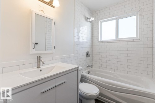 Bathroom featuring a white subway tile surround, a bathtub with an integrated shower, and a vanity with a white countertop and basin sink - 13108 133 Street, Edmonton, AB - Indoor Photo Showing Bathroom