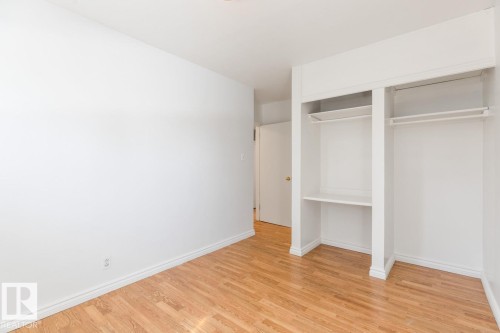 This room features a built-in wardrobe with shelving and hanging rods, light-toned hardwood flooring, and white baseboards - 13108 133 Street, Edmonton, AB - Indoor