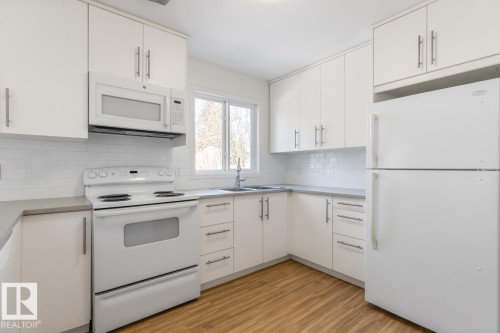 The kitchen features white cabinetry, a white subway tile backsplash, and light wood-look flooring - 13108 133 Street, Edmonton, AB - Indoor Photo Showing Kitchen With Double Sink