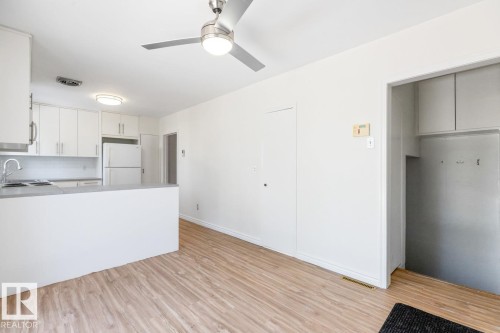 Open concept living area with light-toned flooring, featuring a kitchen with white cabinetry, a refrigerator, and a breakfast bar - 13108 133 Street, Edmonton, AB - Indoor Photo Showing Kitchen