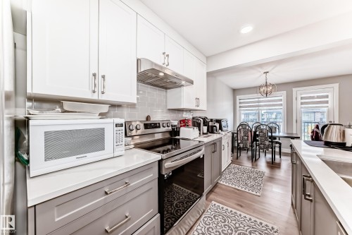 The kitchen features white upper cabinetry, grey lower cabinetry, and stainless steel appliances - 7822 Koruluk Link Link, Edmonton, AB - Indoor Photo Showing Kitchen