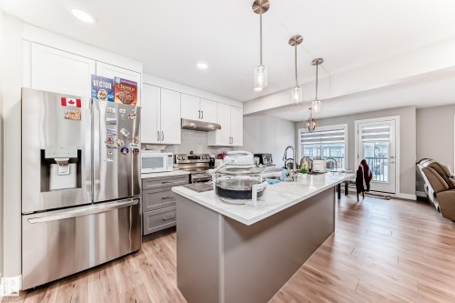 The kitchen features a stainless steel refrigerator, white and grey cabinetry, and a center island with pendant lighting - 7822 Koruluk Link Link, Edmonton, AB - Indoor Photo Showing Kitchen With Upgraded Kitchen