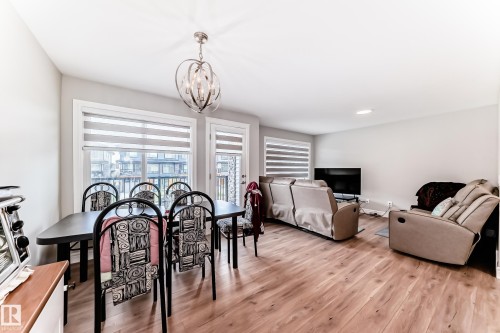 Open concept living and dining area featuring hardwood flooring, a contemporary chandelier, and large windows with blinds - 7822 Koruluk Link Link, Edmonton, AB - Indoor