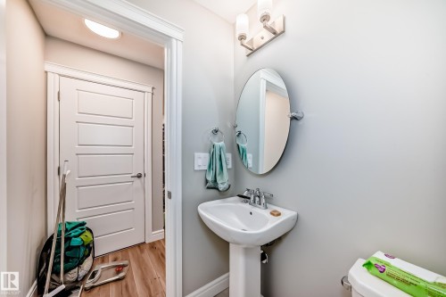 The bathroom features a pedestal sink with a chrome faucet, an oval mirror, and wall-mounted lighting - 7822 Koruluk Link Link, Edmonton, AB - Indoor Photo Showing Bathroom