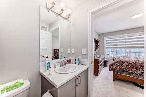 The property features a bathroom vanity with a white countertop and an integrated sink, illuminated by a three-light fixture above a large mirror - 7822 Koruluk Link Link, Edmonton, AB - Indoor Photo Showing Bathroom