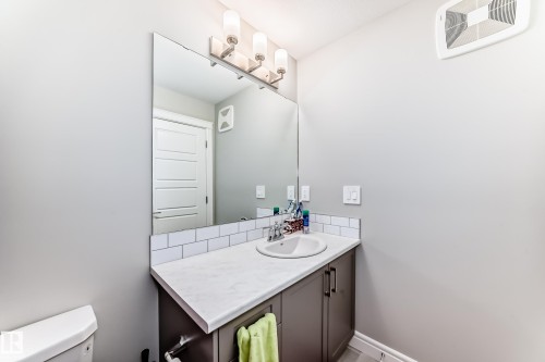 The bathroom features a vanity with a white countertop, an undermount sink, and a large mirror - 7822 Koruluk Link Link, Edmonton, AB - Indoor Photo Showing Bathroom