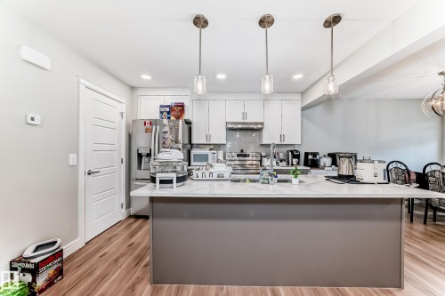 The kitchen features a large island with a light-colored countertop, white cabinetry, and stainless steel appliances - 7822 Koruluk Link Link, Edmonton, AB - Indoor Photo Showing Kitchen With Upgraded Kitchen