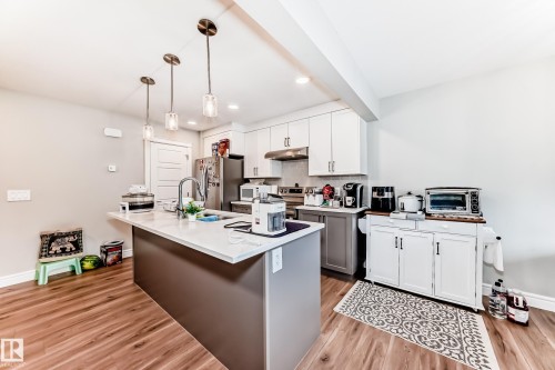 The kitchen features an island with a light-colored countertop, overhead pendant lighting, and warm-toned flooring - 7822 Koruluk Link Link, Edmonton, AB - Indoor Photo Showing Kitchen