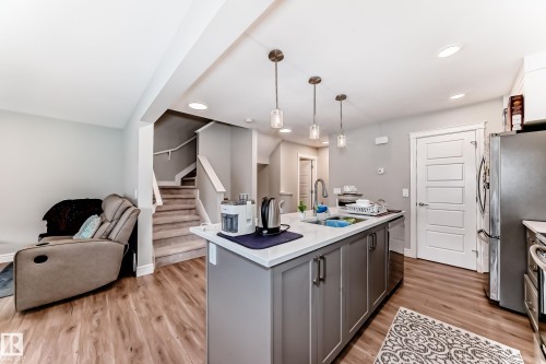 The open concept living area features wood-look flooring, a kitchen island with pendant lighting, and stainless steel appliances - 7822 Koruluk Link Link, Edmonton, AB - Indoor Photo Showing Kitchen With Double Sink With Upgraded Kitchen