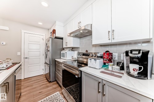The kitchen features light wood tone flooring, white upper cabinetry, and grey lower cabinetry - 7822 Koruluk Link Link, Edmonton, AB - Indoor Photo Showing Kitchen