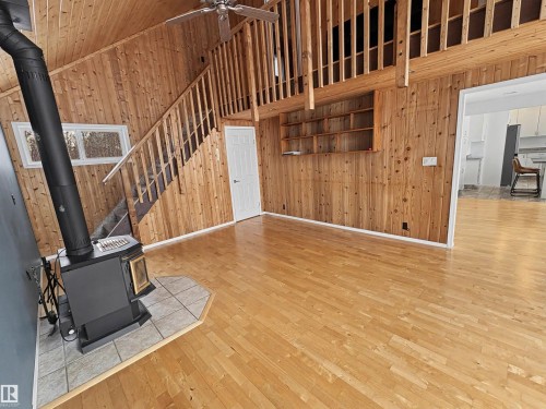 Living area featuring wood paneling on the walls and ceiling, hardwood floors, and a wood-burning stove on a tiled hearth - #4 Kingbird Road, Rural Bonnyville M.D., AB 