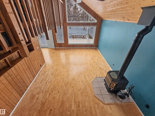 Spacious living area featuring light-toned wood flooring, a striking teal accent wall, and a rustic wood-burning stove with a tiled hearth - #4 Kingbird Road, Rural Bonnyville M.D., AB 