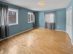 The room features natural wood flooring and three windows providing views of the outdoors - 