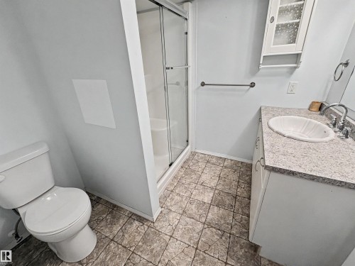Bathroom featuring a vanity with a white countertop and an integrated sink, a toilet, a shower with a glass enclosure, and patterned flooring - #4 Kingbird Road, Rural Bonnyville M.D., AB 