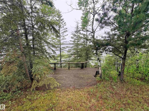 Waterfront wooden deck with integrated bench seating, framed by mature evergreen and deciduous trees - #4 Kingbird Road, Rural Bonnyville M.D., AB 