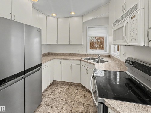 This kitchen features white cabinetry, a double basin sink, and stainless steel appliances, including a refrigerator, microwave, and electric range - #4 Kingbird Road, Rural Bonnyville M.D., AB 