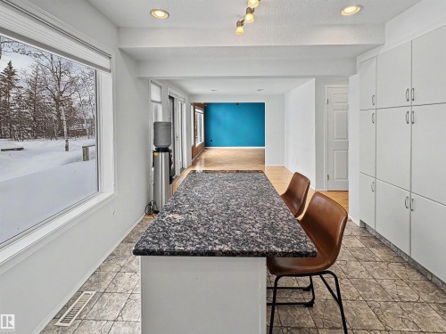 The kitchen area features a spacious island with a dark granite countertop, extensive white cabinetry, and tiled flooring - #4 Kingbird Road, Rural Bonnyville M.D., AB 