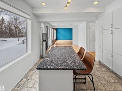 The kitchen area features a spacious island with a dark granite countertop, extensive white cabinetry, and tiled flooring - 