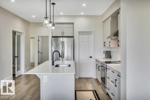 The kitchen features a center island with a sink and pendant lighting, white cabinetry with dark hardware, a stainless steel refrigerator, and a stainless steel range with a coordinating hood - 13007 213 Street, Edmonton, AB - Indoor Photo Showing Kitchen With Upgraded Kitchen