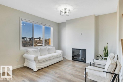 This inviting living space features light-toned flooring, a large window offering exterior views, and an electric fireplace - 13007 213 Street, Edmonton, AB - Indoor Photo Showing Living Room With Fireplace