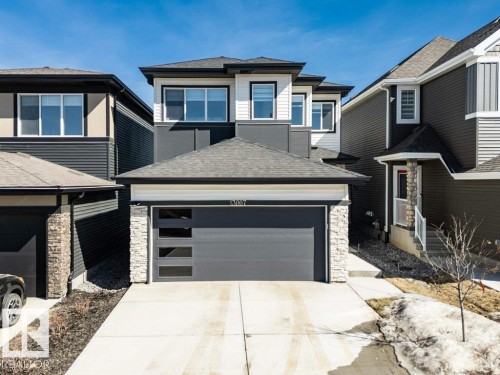 The property features a modern exterior with dark siding and light stone accents, a grey garage door with frosted windows, and a concrete driveway - 13007 213 Street, Edmonton, AB - Outdoor With Facade