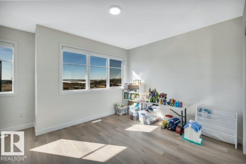 This room features light wood flooring, several windows providing natural light and scenic distant views, and a ceiling light fixture - 13007 213 Street, Edmonton, AB - Indoor