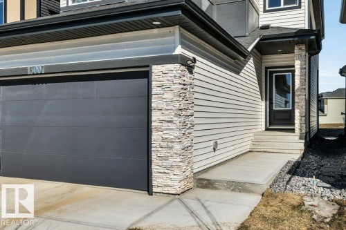 The property features a dark gray garage door, light-colored siding, and stacked stone accents - 13007 213 Street, Edmonton, AB - Outdoor