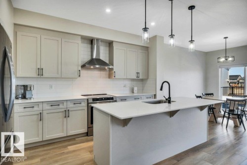 The kitchen features light-toned cabinetry, stainless steel appliances, a white subway tile backsplash, and an island with a sink and pendant lighting - 13007 213 Street, Edmonton, AB - Indoor Photo Showing Kitchen With Upgraded Kitchen