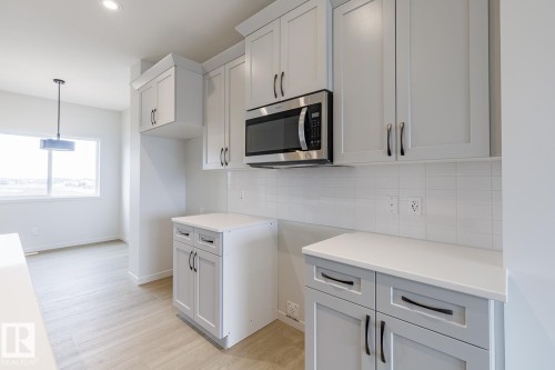 The kitchen features light-colored cabinetry with dark hardware, a stainless steel microwave, and white countertops - 3828 38 Street E, Beaumont, AB - Indoor Photo Showing Kitchen