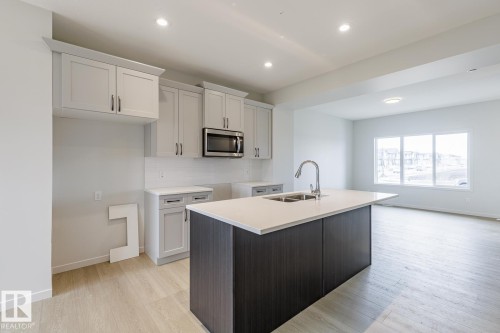 The kitchen features light-colored cabinetry, a built-in microwave, and an island with a sink and a light-colored countertop - 3828 38 Street E, Beaumont, AB - Indoor Photo Showing Kitchen With Double Sink