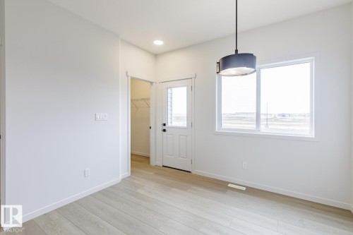 This room features light-colored flooring, a window offering ample natural light, and a modern pendant light fixture - 3828 38 Street E, Beaumont, AB - Indoor Photo Showing Other Room